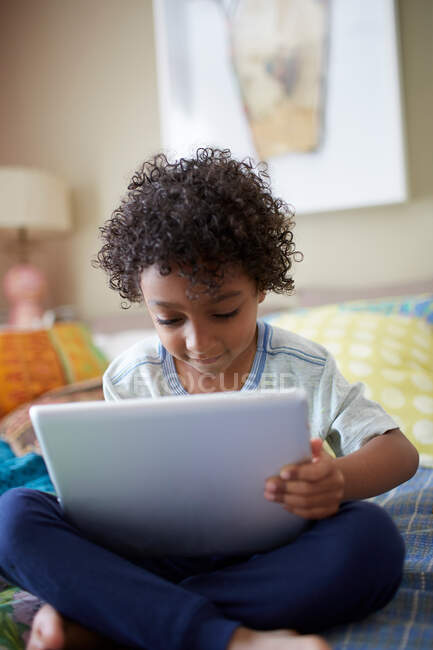 Ребенок сидит на кровати с помощью цифрового планшета — стоковое фото