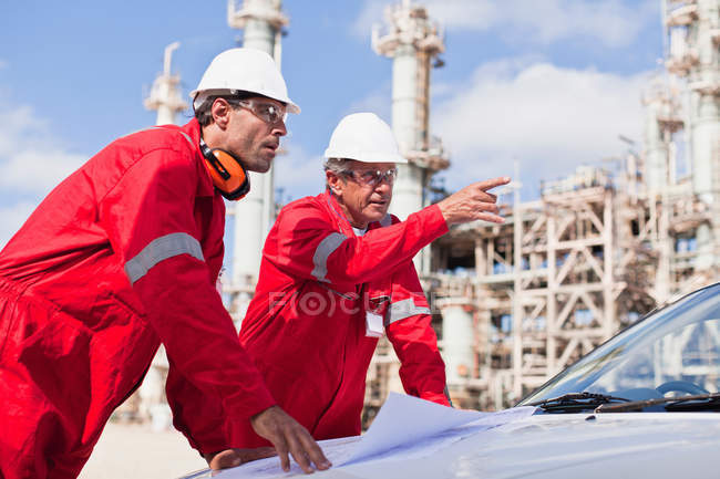 Workers with blueprints at oil refinery — Stock Photo