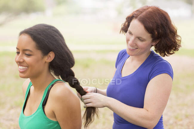 Young woman behind friend plaiting hair smiling — Stock Photo