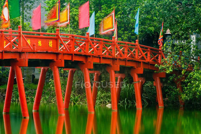 Ponte vermelha sobre ainda riacho em vegetação exuberante — Fotografia de Stock