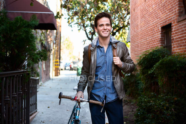 Щасливий молодий чоловік ходить з циклом на тротуарі — стокове фото