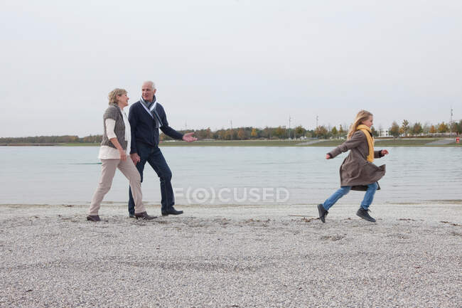 Бабушка с дедушкой и девочка прогуливаются вдоль озера — стоковое фото