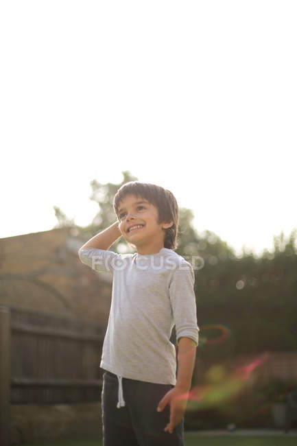 Visão de baixo ângulo do menino no jardim mão na cabeça olhando para longe sorrindo — Fotografia de Stock