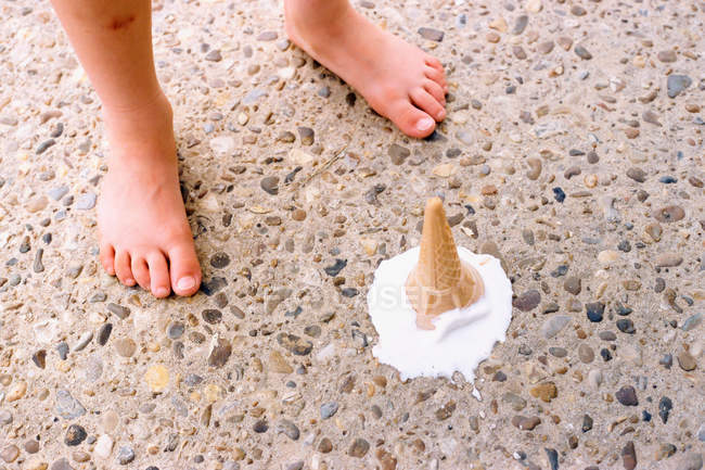 Melting ice cream beside kid feet — Stock Photo