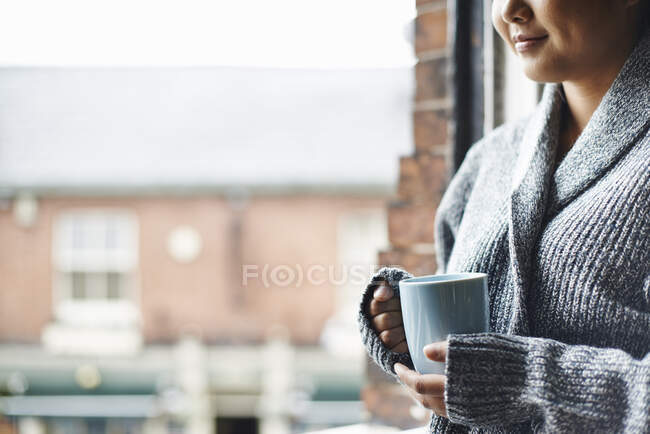 Mujer joven en cocina sosteniendo taza de café - foto de stock