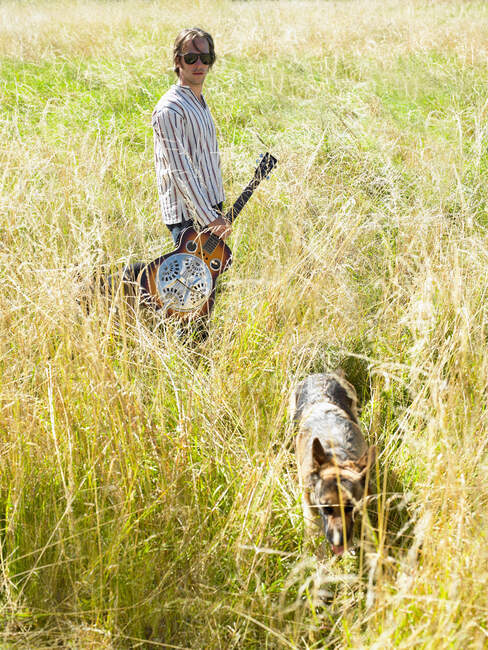Homme avec sa guitare et son chien dans un champ — Photo de stock