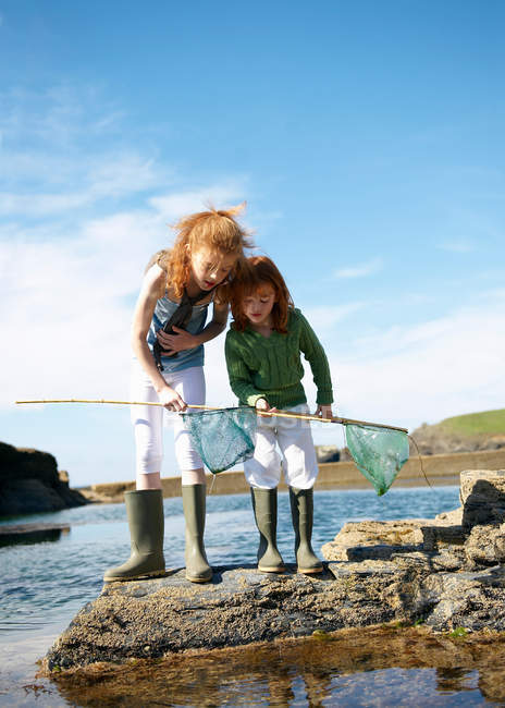 2 girls looking in nets at rock pool — Stock Photo