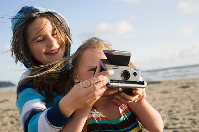 Девушка показывает другу, как использовать мгновенную камеру на пляже — стоковое фото