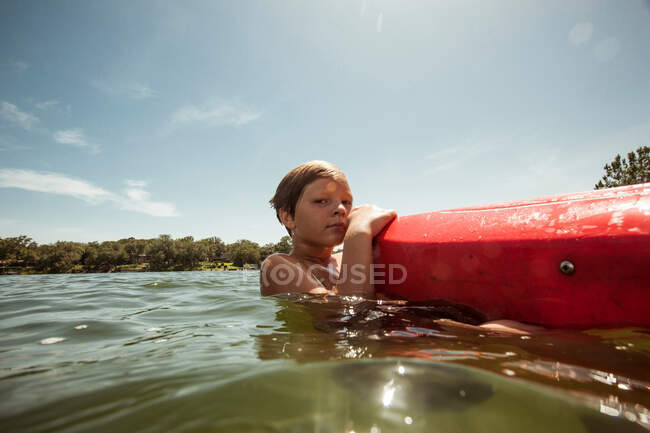 Niño en el agua aferrándose a kayak - foto de stock