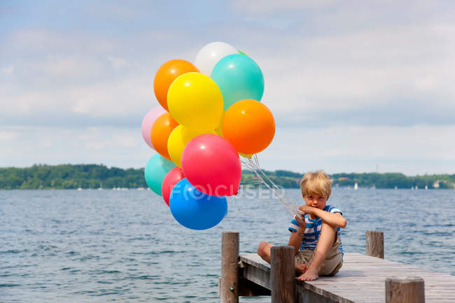 Boy holding balloons on wooden pier — Stock Photo