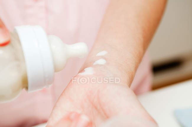 Mother testing baby milk on wrist, close-up partial view — Stock Photo