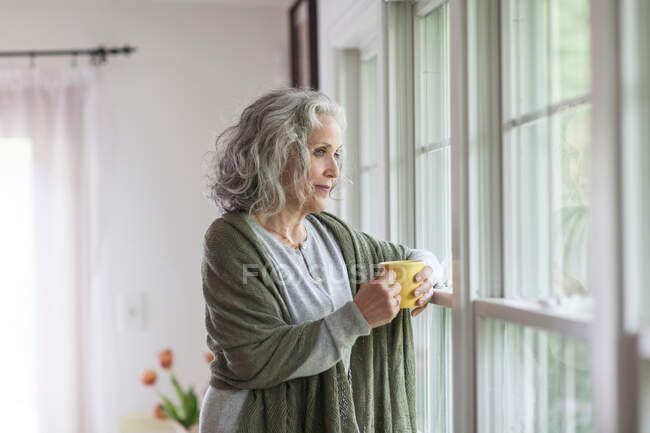Donna anziana che guarda fuori dalla finestra — Foto stock