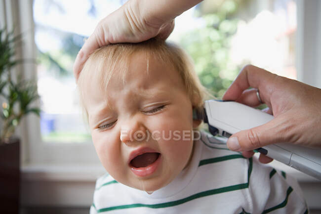 Adult putting thermometer in ear of crying baby — Stock Photo