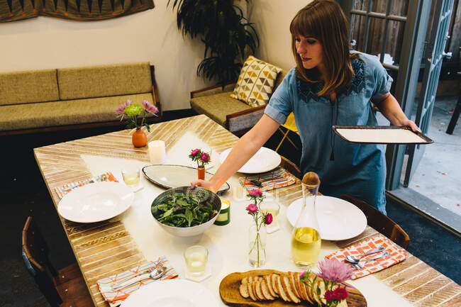 Mujer colocar el plato en la mesa de comedor - foto de stock