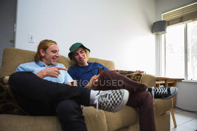 Два молодых человека сидят на диване и смотрят на смартфон. — стоковое фото