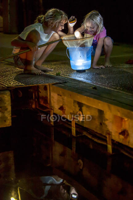 Girls crouching on pier and looking into bucket — Stock Photo