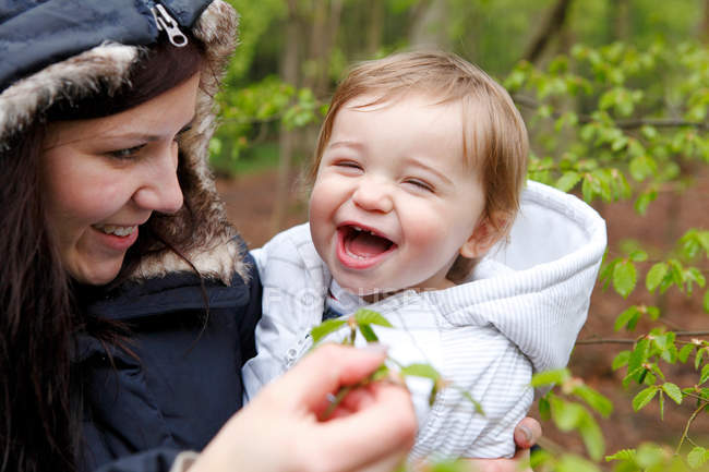 Sonriente madre llevando hijo en el bosque - foto de stock