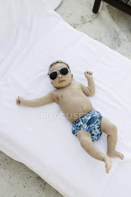 Baby with sunglasses lying on mattress — Stock Photo