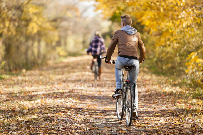 Rear view of teenage boy and adult sister cycling in autumn forest — Stock Photo