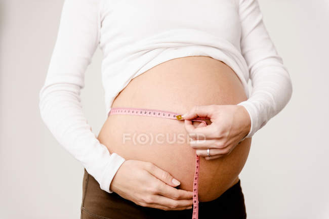 Cropped image of pregnant woman measuring her belly — Stock Photo