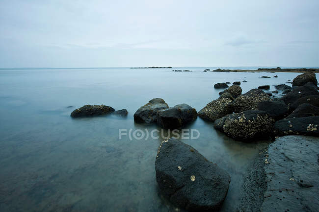 Rocas en aguas tranquilas de la costa - foto de stock