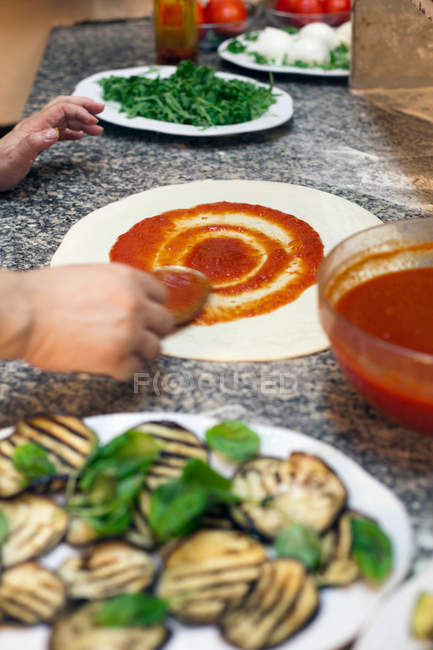 Koch verteilt Sauce auf Pizzateig — Stockfoto