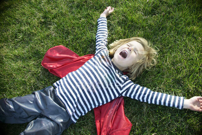 Мальчик в красной накидке, притворяющийся летать — стоковое фото