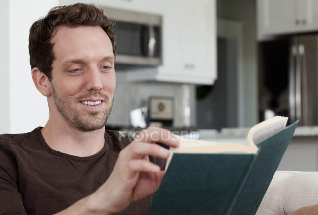 Середній дорослий чоловік сидить удома, читає книгу — стокове фото