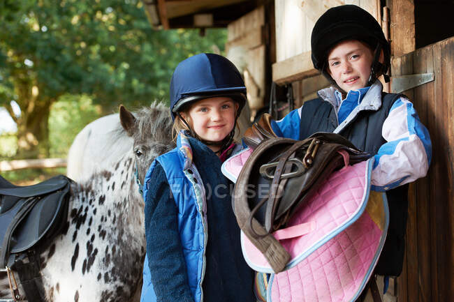 Zwei Mädchen halten Sättel mit Pony — Stockfoto