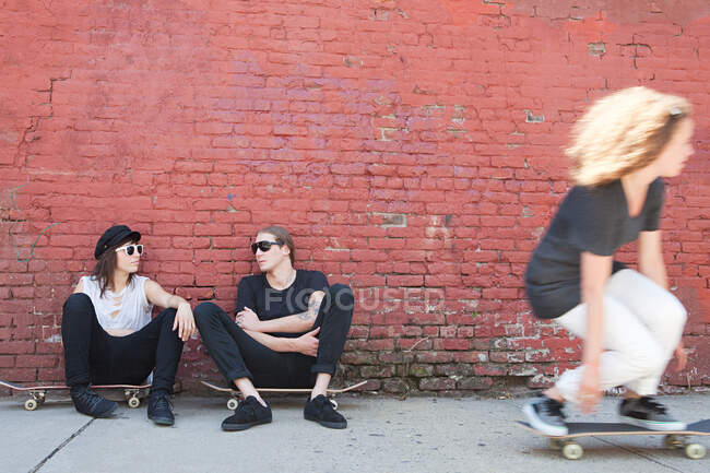 Skaters sitting on boards as other skater goes past — Stock Photo