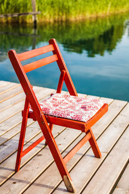 Chair on wooden pier beside lake in sunlight — Stock Photo