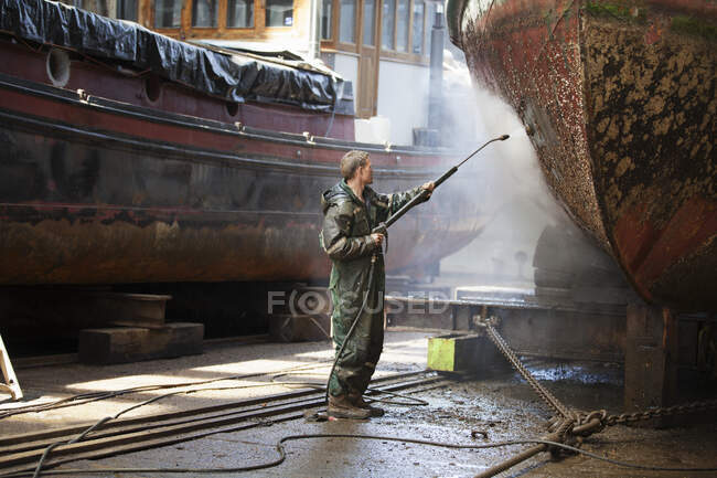 Працівник очищення човна з шлангом високого тиску на верфі — стокове фото