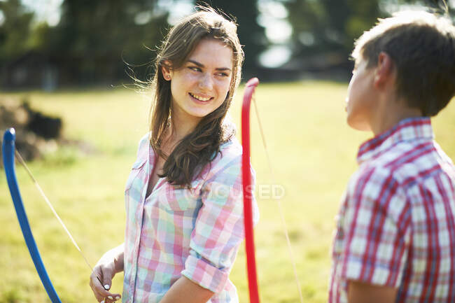 Adolescente hablando con su hermano mientras practica tiro con arco - foto de stock