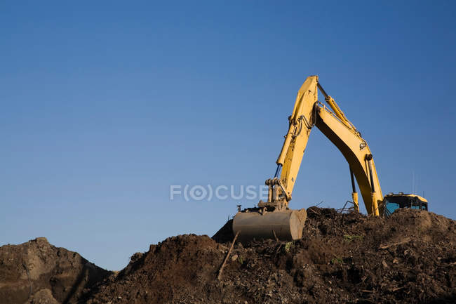 Bagger arbeitet bei klarem Himmel an Mutterboden-Haufen — Stockfoto