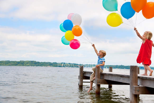 Children holding balloons on wooden pier — Stock Photo