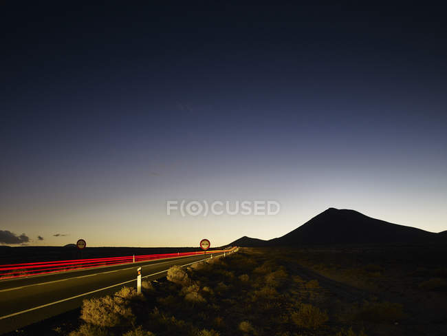 Senderos de luz trasera de carretera al amanecer con silueta de montaña - foto de stock