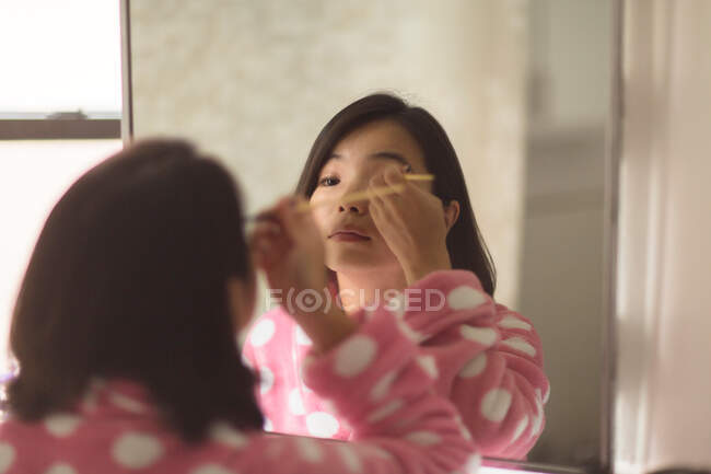 Young woman applying makeup using bathroom mirror — Stock Photo