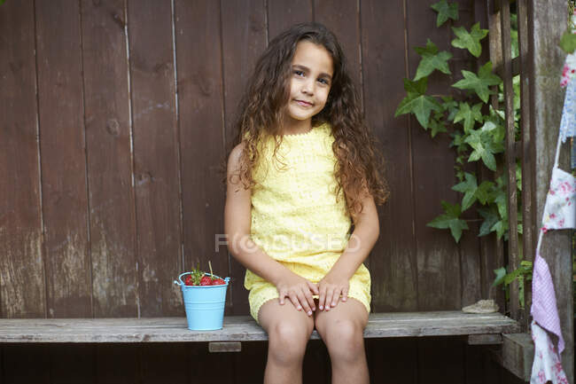 Retrato de menina sentada no banco com um balde de morangos frescos — Fotografia de Stock