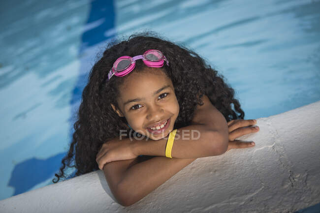Портрет дівчини з кучерявим чорним волоссям, що висить на краю басейну, дивлячись на камеру, що посміхається — стокове фото