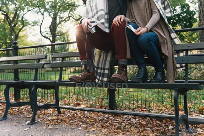 Vista del cuello hacia abajo de una pareja adulta envuelta en una manta sosteniendo una cámara instantánea en el parque - foto de stock