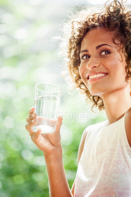 Mujer sonriente bebiendo vaso de agua - foto de stock