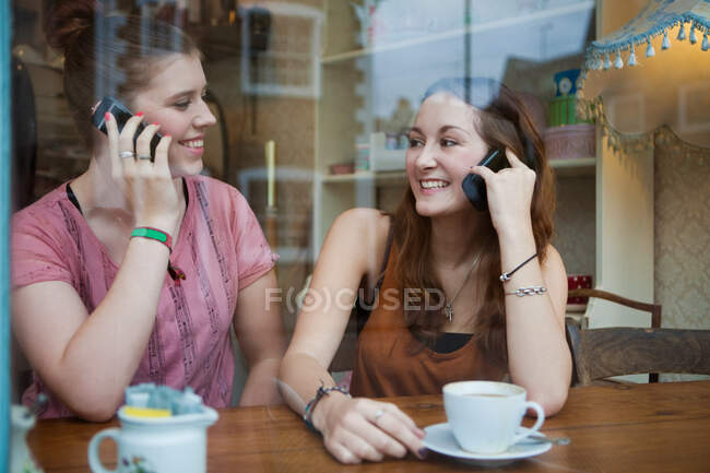 Mujeres jóvenes en la cafetería en los teléfonos celulares - foto de stock