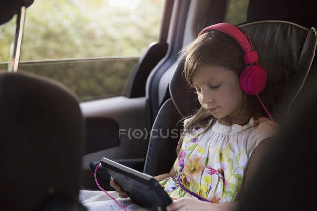 Girl wearing pink headphones using digital tablet in car — Stock Photo