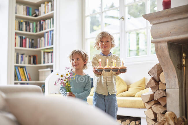 Two boys holding flowers and cupcakes with lit candles — Stock Photo