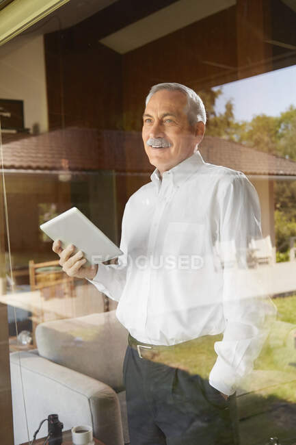 Homme âgé à la maison, tenant une tablette numérique — Photo de stock