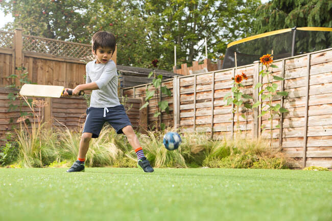 Мальчик играет в крикет в саду, мяч в воздухе — стоковое фото
