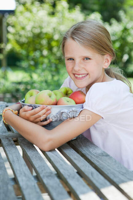 Menina abraçando uma tigela cheia de maçãs — Fotografia de Stock