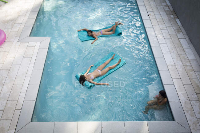 Vista de ángulo alto de dos mujeres tomando el sol en inflables en la piscina, Santa Rosa Beach, Florida, EE.UU. - foto de stock