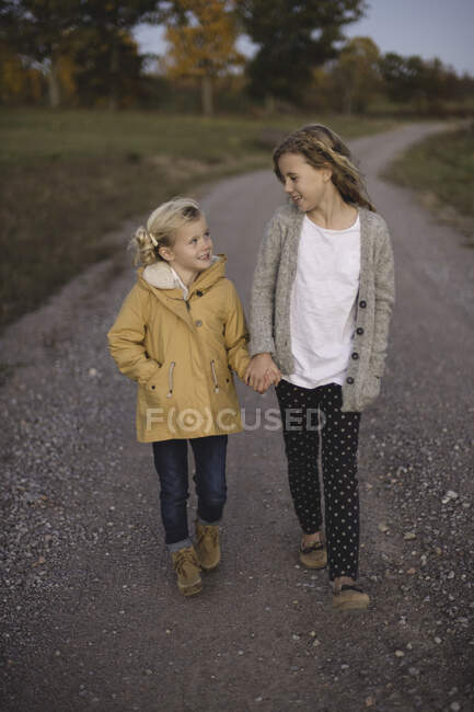 Dos chicas jóvenes caminando por el camino del campo, de la mano - foto de stock