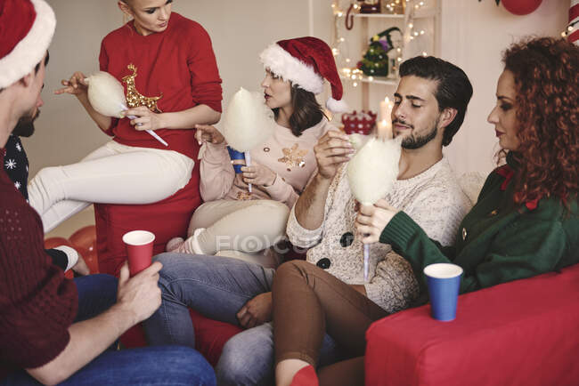 Молоді жінки і чоловіки їдять цукерки на дивані на різдвяній вечірці — стокове фото